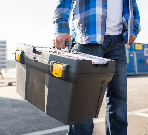 Worker holding a toolbox while walking on a sauna construction site.