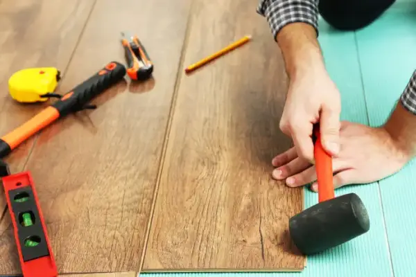 Installer tapping SPC flooring planks into place with mallet.