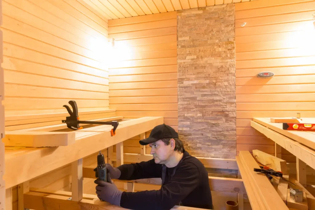 Worker assembling a sauna with wooden benches and stone heater