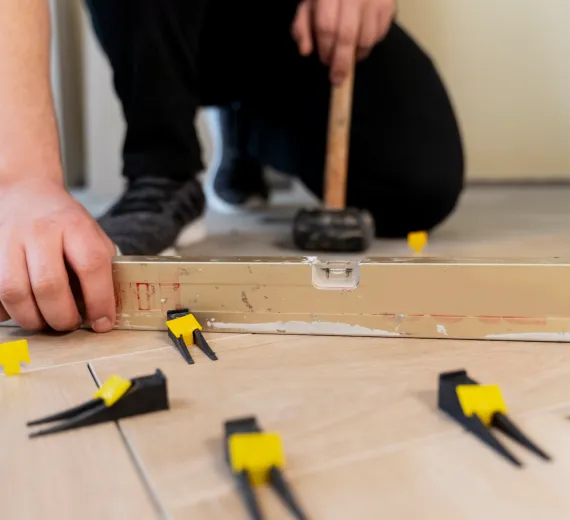 Person using a hammer to adjust LVT floor tiles.