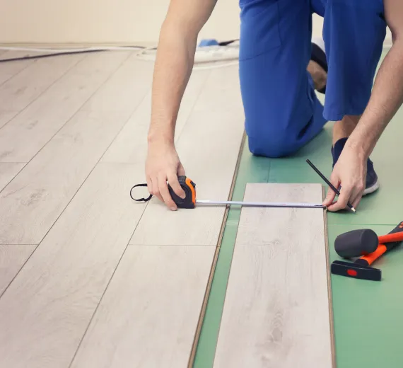 Installer measuring SPC flooring planks with tape measure.
