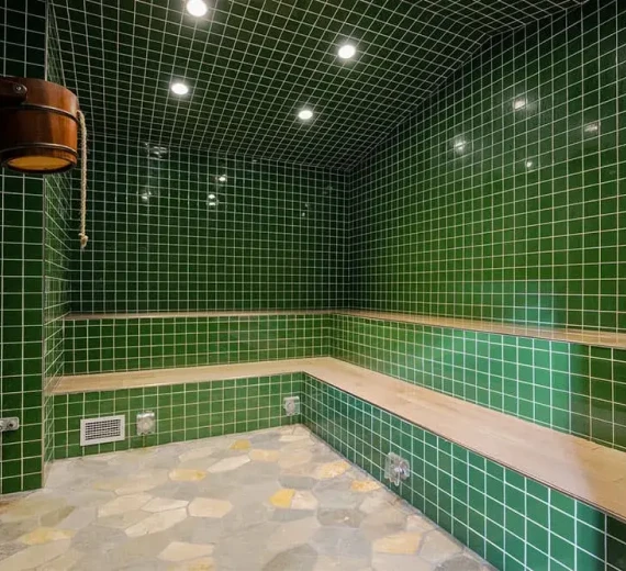 Steam room with green tiles, wooden benches, and calming lighting.