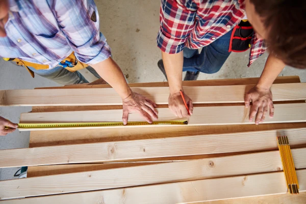 Professionals measuring wooden floorboards with a tape measure.