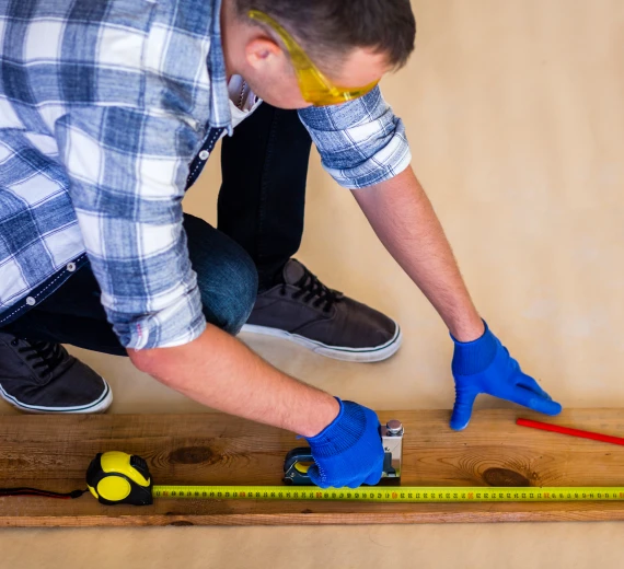 Installer measuring wooden planks with tape measure and pencil.